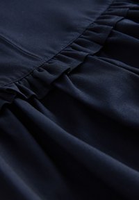 Tumesinine tekstiil, mille serval on kogutud volangisõlm, sile ja veidi tekstuuriga kangaspind.