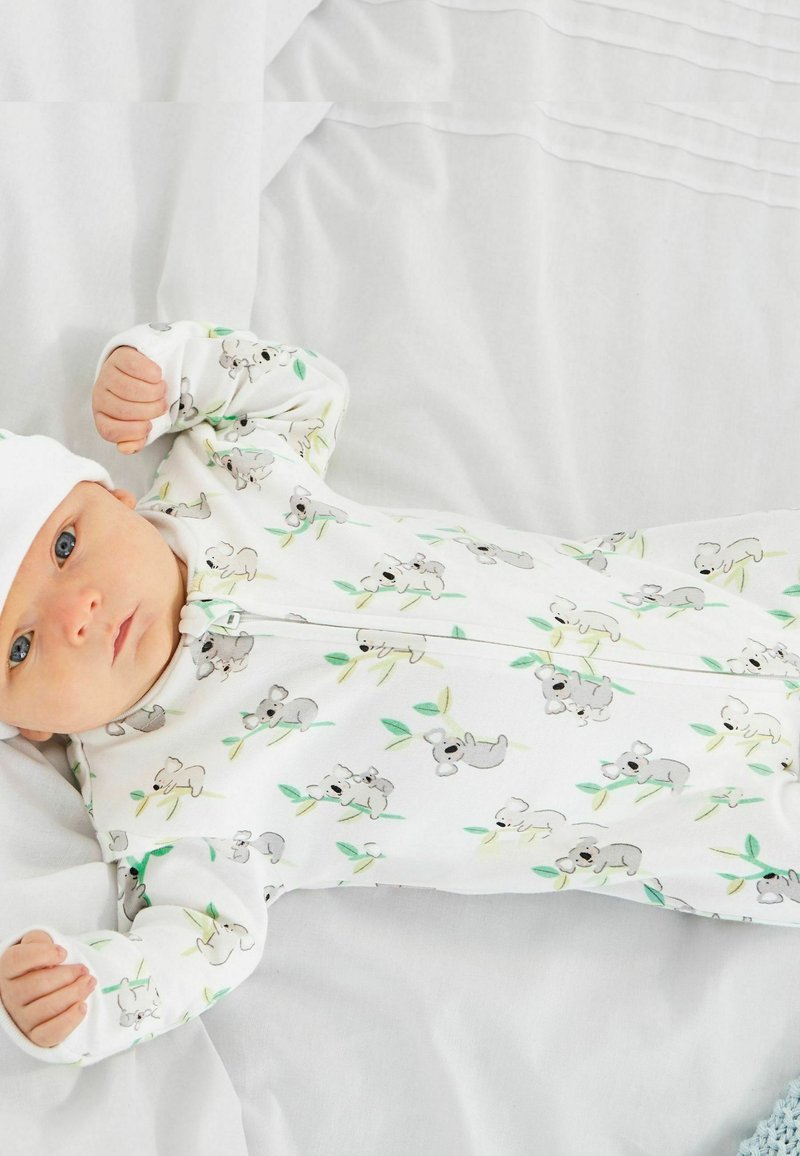 Valkoinen vetoketjullinen haalari, jossa on koalan kuva harmailla ja vihreillä yksityiskohdilla, valmistettu pehmeästä kankaasta, ja sitä on täydennetty sopivalla valkoisella myssyllä.