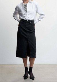 Jupe en denim noire avec une coupe droite, fente à l'avant et fermeture à boutons, associée à une chemise blanche à boutons et un haut rayé. Chaussettes noires et talons.