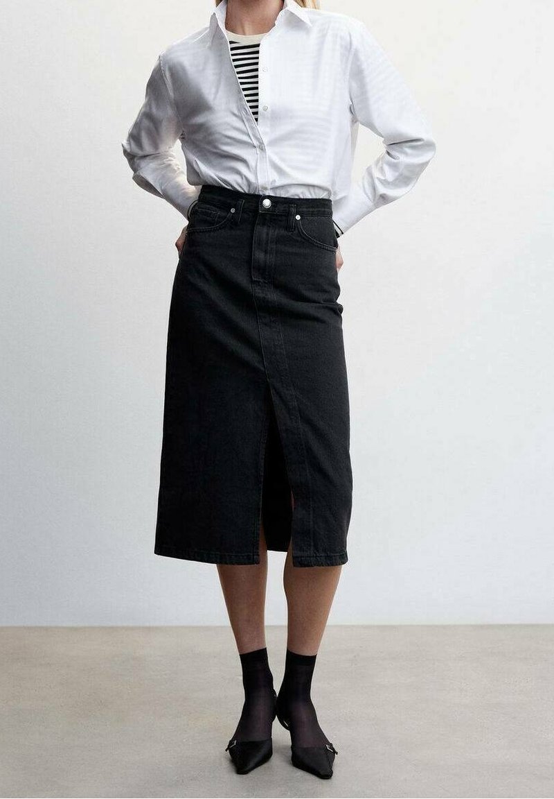 Jupe en denim noire avec une coupe droite, fente à l'avant et fermeture à boutons, associée à une chemise blanche à boutons et un haut rayé. Chaussettes noires et talons.