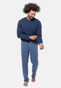 T-paita merivoimansinisellä pitkähihaisella V-pääntiellä, jossa on rintatasku, yhdistettynä siniruutuisiin pyjamahousuihin, joissa on joustava vyötärö ja löysä istuvuus.