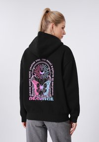 Sweat à capuche noir avec cordon de serrage. Le dos présente un graphisme coloré avec un soleil, une lune, un papillon et du texte. Tissu doux, coupe décontractée.