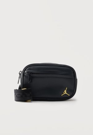 Fekete téglalap alakú oldaltáska elülső cipzáras zsebbel, állítható pánttal és arany színű Jumpman logóval az alsó jobb sarokban.