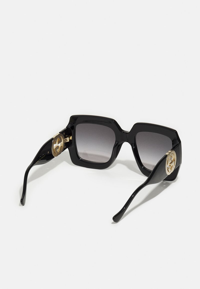 Black square sunglasses with gradient lenses, featuring gold logo accents on the sides and a glossy plastic frame.