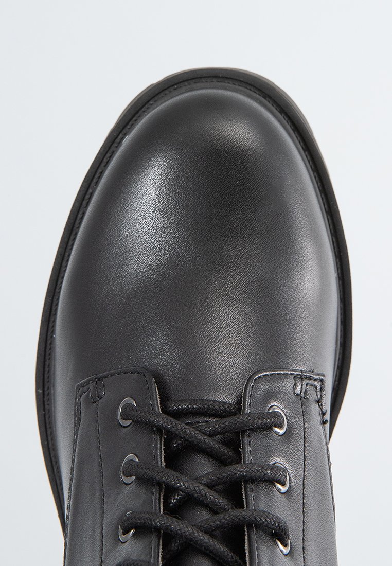 Schwarzer Lederstiefel mit glatter Oberfläche, runder Zehenpartie, acht metallischen Ösen und flachen Schnürsenkeln, die eine detaillierte Nahtführung entlang der Nähte zeigen.