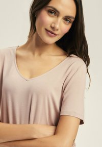 Jasnoróżowa bluzka na krótki rękaw z dekoltem w kształcie litery V. Miękka tekstura, luźny krój. Podkreśla dekolt i ramiona, bezszwowy design.