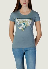 Svijetloplava majica s trokutastim grafičkim dizajnom s cvjetnim detaljima i riječi "GUESS?" u sredini, kratkih rukava, od pamuka.