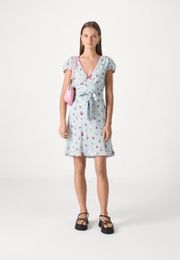 Rochie florală de culoare bleu deschis, cu mâneci scurte tip puff, decolteu adânc în formă de V, talie legată și accente roșii; asortată cu o poșetă mică roz și sandale negre.