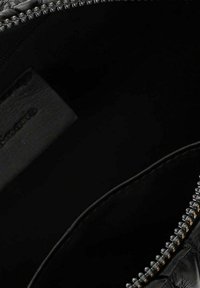 Innenansicht einer schwarzen Leder-Tasche mit Reißverschluss, sichtbaren Nähten und einem an das Innenfutter genähten Stoffetikett.