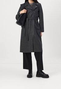 Grå uldblanding frakke med bælte i taljen, lynlåslukning foran og klapkrave. Sammen med sorte vide bukser og kraftige sorte støvler.