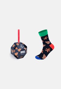 Caja de regalo negra con cinta roja, decorada con galletas de jengibre y motivos navideños. Calcetín colorido con fondo oscuro, estampado de galletas de jengibre y puños de colores.