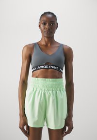 Pilkas sportinis liemenukas su iškirpimo detale ir juodu "Nike Pro" juostos akcentu, derinamas su šviesiai žaliais, tampriais šortais, turinčiais elastingą juosmenį.