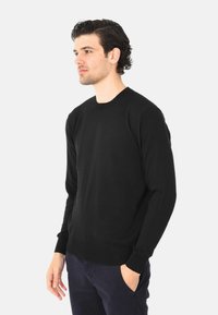 Maglione nero a girocollo realizzato in tessuto morbido, con maniche lunghe e polsini e orlo a costine. Indossato con pantaloni scuri.