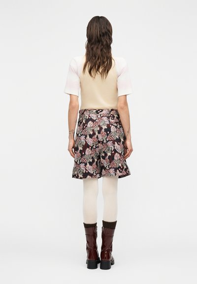 Φλοράλ φούστα σε σκούρο ύφασμα με ροζ και πράσινα σχέδια, συνδυασμένη με κρεμ καλσόν και καφέ μποτάκια με τακούνι. Αμάνικο ανοιχτόχρωμο τοπ.