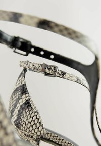 Aukštakulniai sandalai su juodai balta gyvatės odos raštu. Su blizgia juoda juostele ir metaliniu sagties detalė.