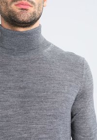 Maglione grigio a collo alto con design aderente, texture a costine al collo e tessuto a maglia morbida.
