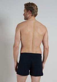 Pantalones cortos de algodón negros con una cinturilla elástica, vistos desde atrás. El material parece suave con un diseño sencillo y sin patrones visibles.
