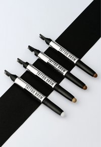 Quattro pennarelli per sopracciglia Tattoo Brow disposti su una superficie nera, con colori variabili: marrone scuro, marrone chiaro, taupe e bianco. Ognuno ha una punta texturizzata.
