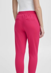 Úzké růžové joggers vyrobené z měkkého materiálu, s elastickým pasem a dvěma zadními kapsami s hladkým povrchem.