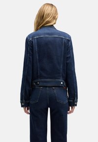 Ciemna kurtka dżinsowa o dopasowanym kroju, z guzikami jako akcentami, klasycznym kołnierzem oraz widocznym przeszyciem na plecach.