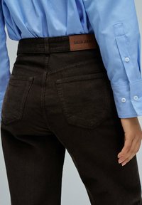 Pantalones de pana marrón con un acabado texturizado, que cuentan con un parche de cuero de Salsa Jeans en la cinturilla y dos bolsillos traseros.