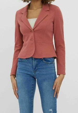 Woman wearing a fitted, dusty pink blazer with two buttons over a white top and blue high-waisted jeans with slight distressing.