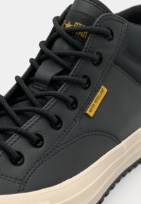 Baskets imperméables grises avec cuir texturé, lacets noirs ronds, œillets et semelle en caoutchouc crème. Détail de tag jaune "WATER REPellent".