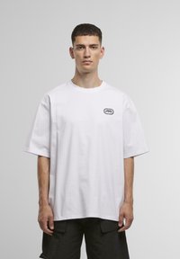 Hvid bomulds T-shirt med korte ærmer, rund hals og et gråt logo på venstre brystområde; afslappet pasform, glat tekstur.