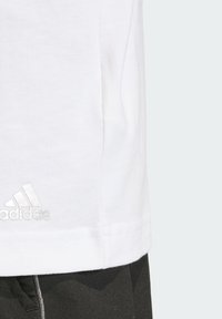 Biela bavlnená tričko s rovnými strihom, s lesklým logom Adidas na boku. Hladká textúra, minimalistický dizajn.