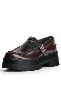 Braune Leder-Plateauschuhe mit einer runden Zehenpartie, ausgestattet mit einem seitlichen Riemen mit Schnalle und dekorativen Nähten entlang des Obermaterials. Dicke schwarze Sohle.