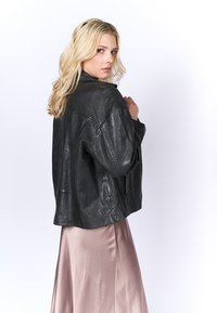 Giubbotto di pelle nera con vestibilità ampia, caratterizzato da un ampio colletto e maniche leggermente oversize, abbinato a una gonna di satin rosa chiaro.