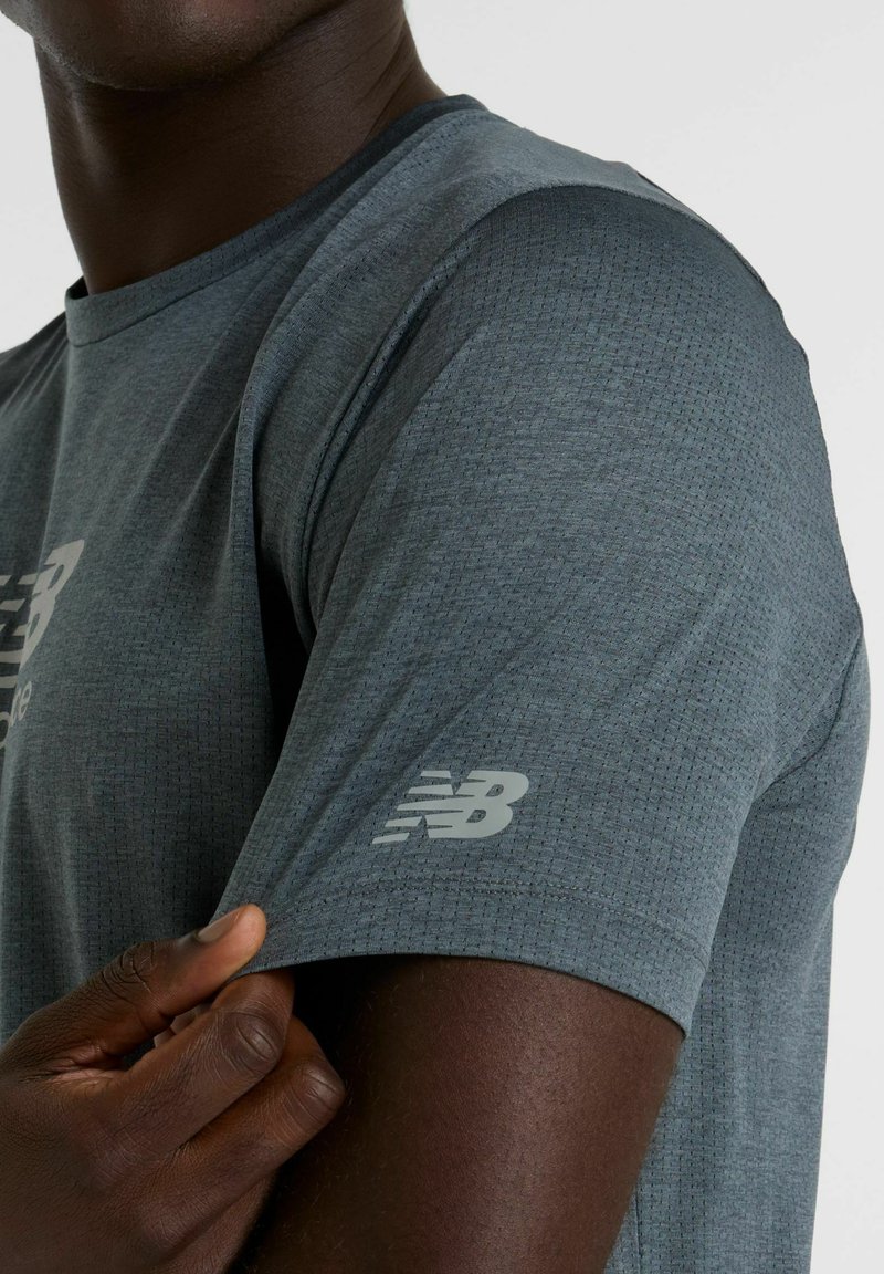 Gray athletic t-shirt with textured fabric and short sleeves. Features a reflective "New Balance" logo on the right sleeve.