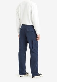 Marineblauwe cargobroek gemaakt van katoen, met zijzakken en achterkleppen, gecombineerd met een wit shirt met lange mouwen en zwarte sneakers.