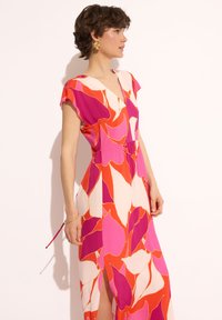 Kolorowa długa sukienka w różowy, czerwony i biały kwiatowy wzór z dekoltem w kształcie V, krótkimi rękawami i bocznymi rozcięciami dla luźniejszego fasonu.