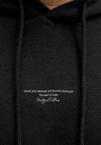 Czarna bluza z kapturem z białym napisem na piersi: "Wyspy z herbaciarniami i pięknymi krajobrazami, Serce Japonii, Dziedzictwo i Tradycje".