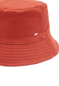 Kapelusz typu bucket w kolorze rdzy z korduroju. Posiada poziome żebrowane tekstury oraz małą metalową metkę z logo. Miękka tkanina i szeroki brzeg.