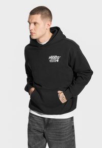 Czarna bluza z kapturem z kieszenią z przodu, ozdobiona bia�łym nadrukiem na piersi, wykonana z miękkiego, teksturowanego materiału.