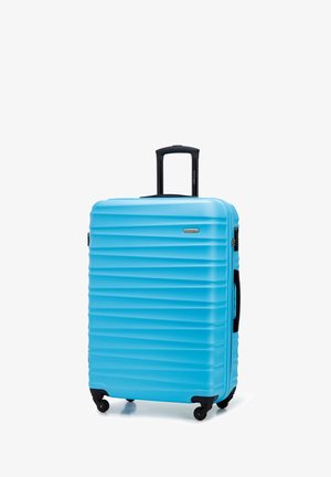 Valise rigide bleue à motifs ondulés avec poignée noire rétractable, poignée latérale et quatre roulettes noires.