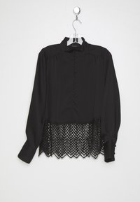 Svart skjorta med hög halsringning, knäppning och långa ärmar, med en spetskant i nederkant som skapar en scalloped kant.