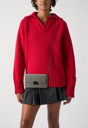 Rode gebreide trui met een v-hals en geribde manchetten, gecombineerd met een zwart-witte houndstooth schoudertas met een zilveren kettingriem.