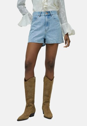 Shorts de mezclilla con un lavado azul claro, diseño de cintura alta y cuatro bolsillos, combinados con botas de vaquero altas de ante marrón con detalles de costura.