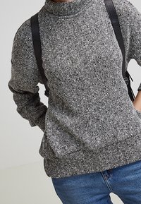 Grå melerad stickad tröja med hög halsringning, med ribbade ärmslut och nederkant; bärs tillsammans med blå denimjeans och en svart axelväska.