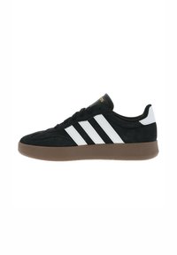 Sneaker in suede nero con tre strisce bianche sul lato, suola in gomma marrone e lacci neri. Presenta un colletto imbottito e un logo dorato.