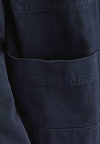 Dark denim fabric featuring a chest pocket, clean stitching, and a solid color design, highlighting a smooth texture and structured shape.