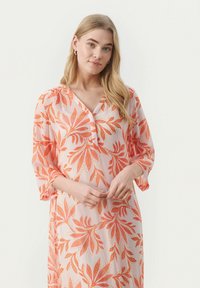Blommig klänning i genomskinligt tyg, med en rosa bas och orange bladmönster, V-ringning och trekvartsärmar. Lätt och svävande design.