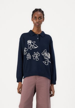 Granatowy sweter polo z dzianiny z białym haftem w kwiaty, kołnierzykiem i luźnym krojem. Połączenie z jasnoróżowymi spodniami dla spójnego wyglądu.