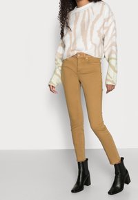 Beige vzorovaný svetr s volným střihem, doplněný o přiléhavé béžové kalhoty a černé kožené kotníkové boty na podpatku. Hladké textury a kontrastní barvy.