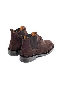 Bottes chelsea en suede marron avec panneaux élastiques sur les côtés, doublure en cuir et une semelle en caoutchouc noir robuste. Elles sont dotées d'un tirant à l'arrière.