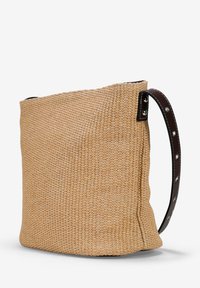 Bolso de mano de paja tejido en beige con un asa de cuero marrón suave que presenta tachuelas plateadas. Forma rectangular con una superficie texturizada.