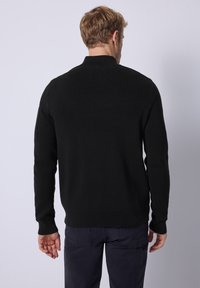 Suéter negro de punto con un alto cuello, diseño ajustado y mangas largas. Presenta puños y dobladillo acanalados, textura suave y sin patrones.
